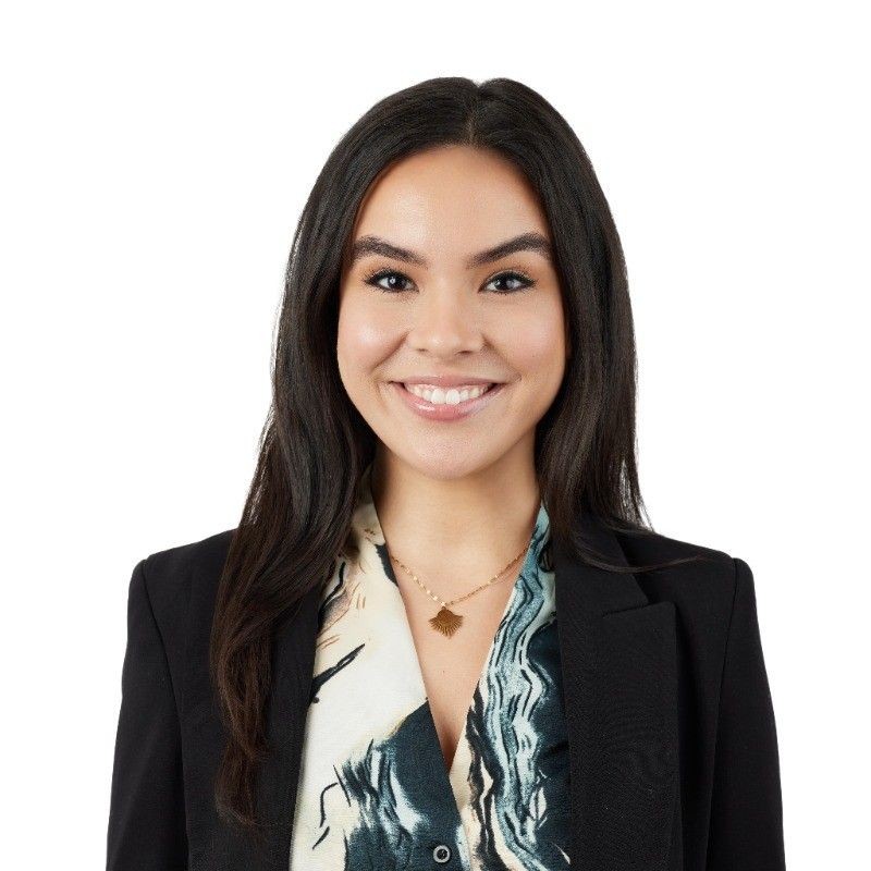 Raquel Quintana with long black hair wearing a black blazer over a patterned blouse and a gold necklace.