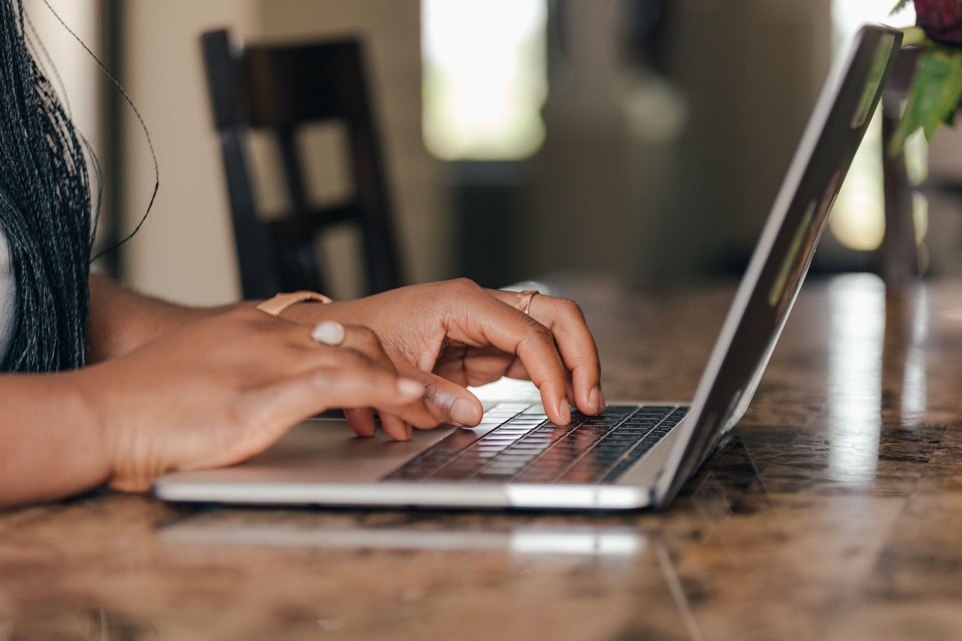 Close-up of hands typing on a laptop keyboard placed on a marble surface with a blurred background.